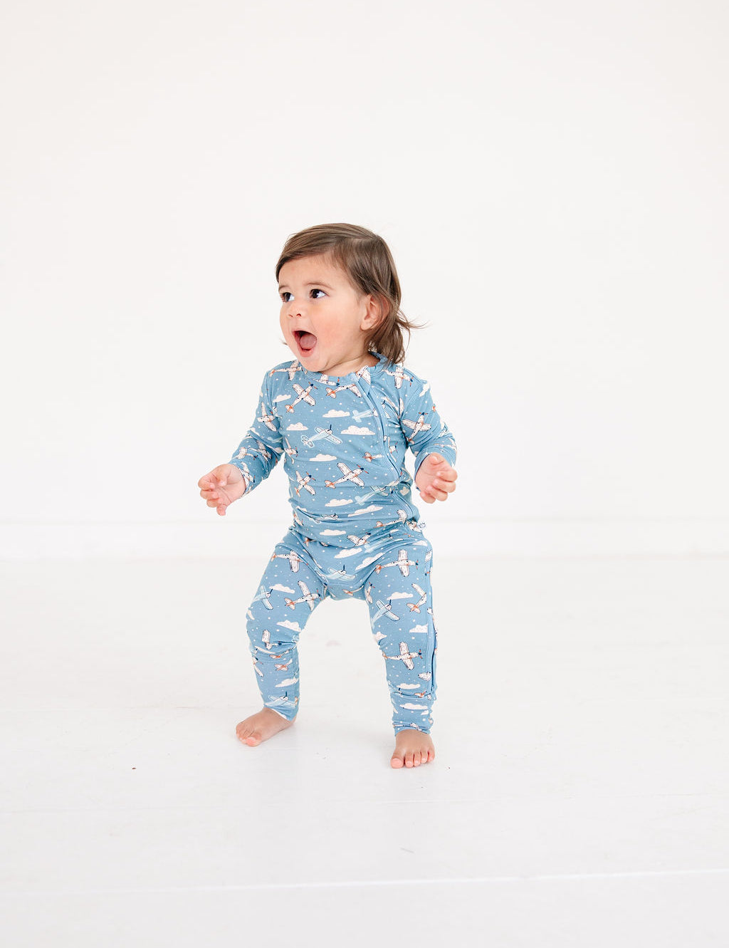 Child wearing a blue pajama with airplane pattern on a white background