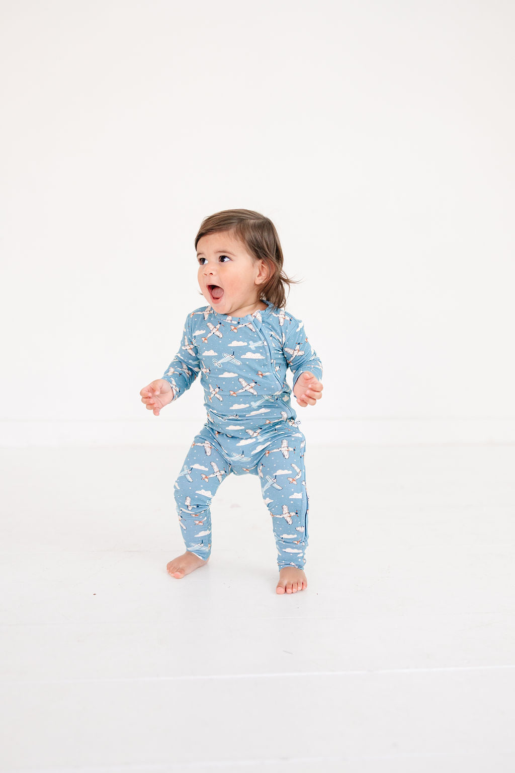 Child wearing a blue pajama with airplane pattern on a white background
