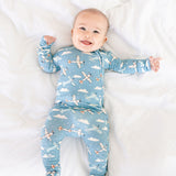 Baby wearing a blue airplane and cloud patterned onesie on a white blanket