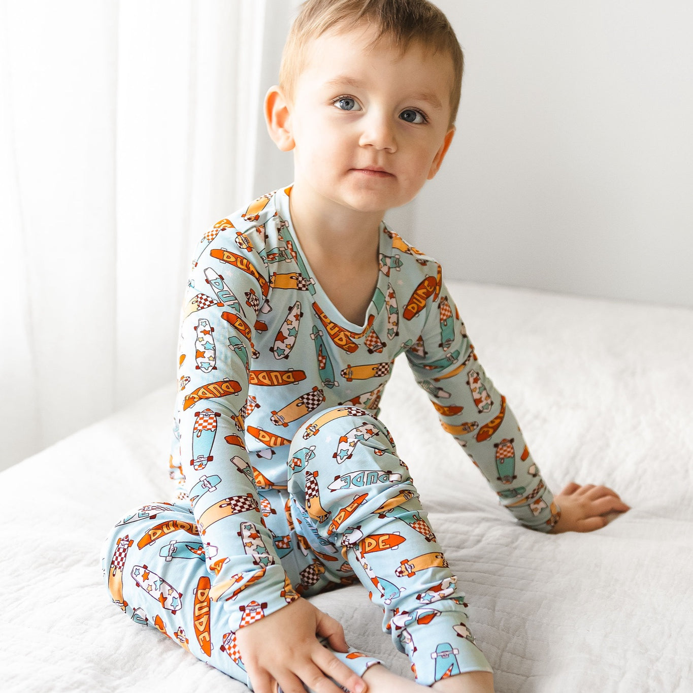 Kaizen Baby Skater Dude Two-Piece PJs bamboo pajamas - Toddler seated on bed, blue skateboard two-piece